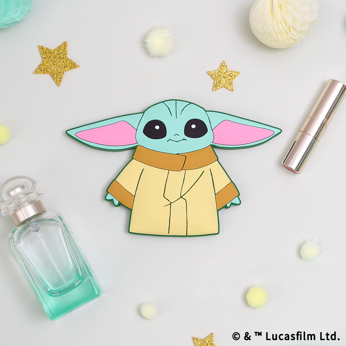 Front view of a Grogu-shaped compact mirror featuring a cartoon Grogu design placed with perfume, lipstick, and decorative stars.