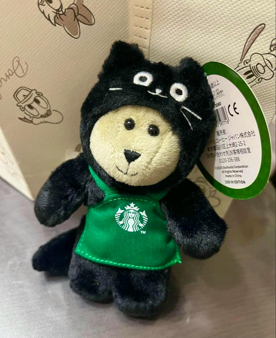 Front view of the Starbucks Bearista black cat plush keychain wearing a green Starbucks apron with its tag visible.
