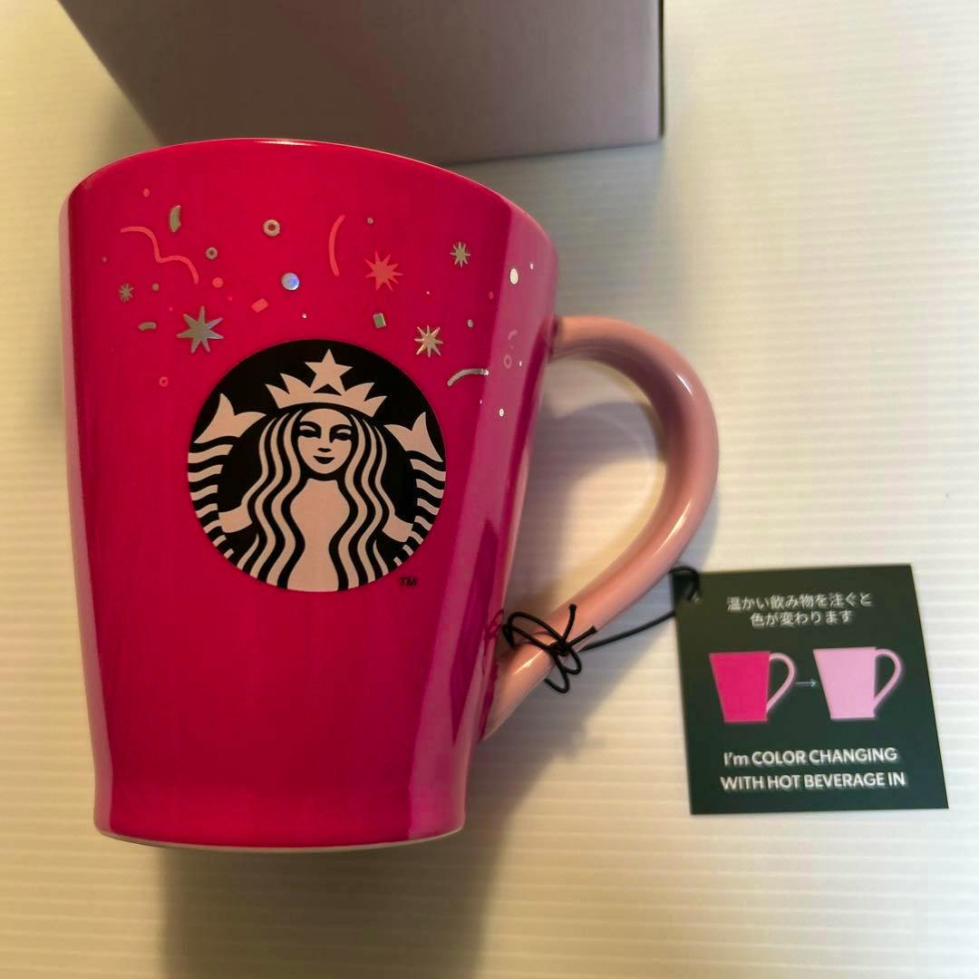 A bright pink Starbucks color-changing mug showing the siren logo, a pink handle, confetti decorations, and an attached tag.
