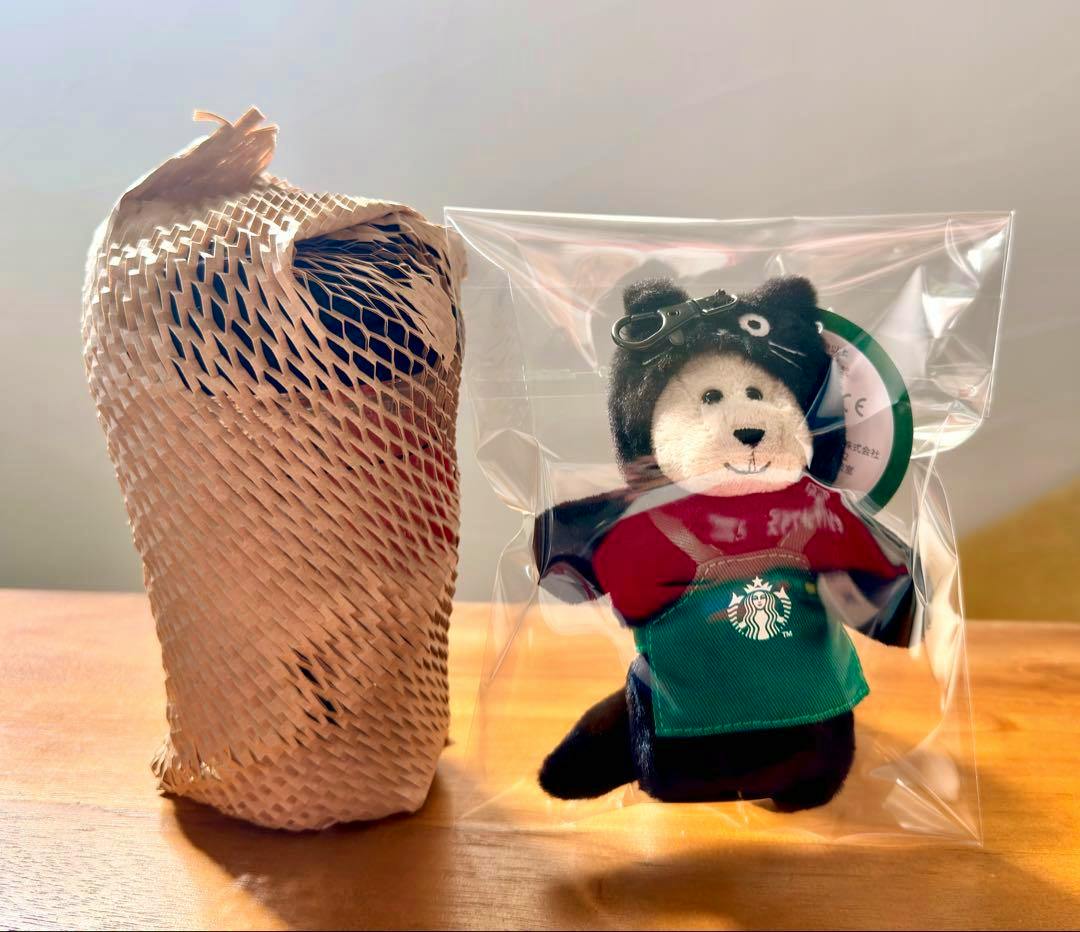 A wrapped double-wall glass in protective mesh sits next to a Starbucks Bearista mini plush in a clear plastic bag.