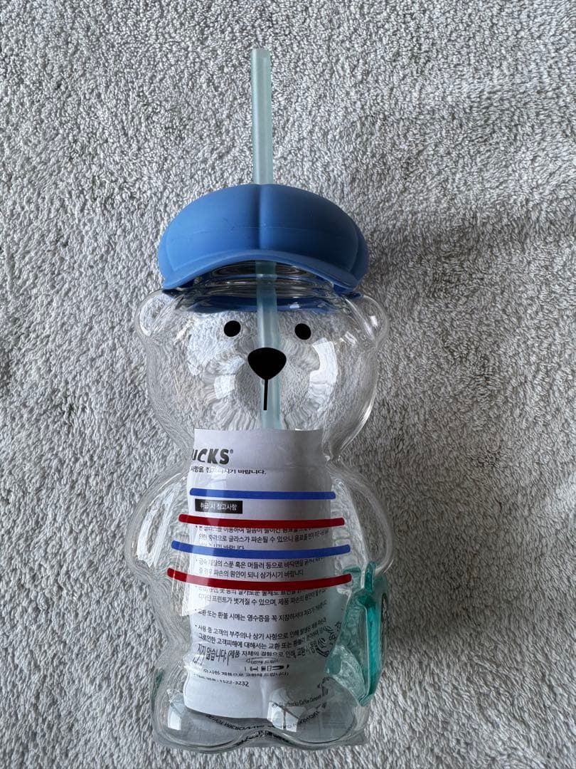 Front view of a clear bear-shaped glass tumbler with a blue lid and straw, matching the Starbucks Korea Bearista glass tumbler.