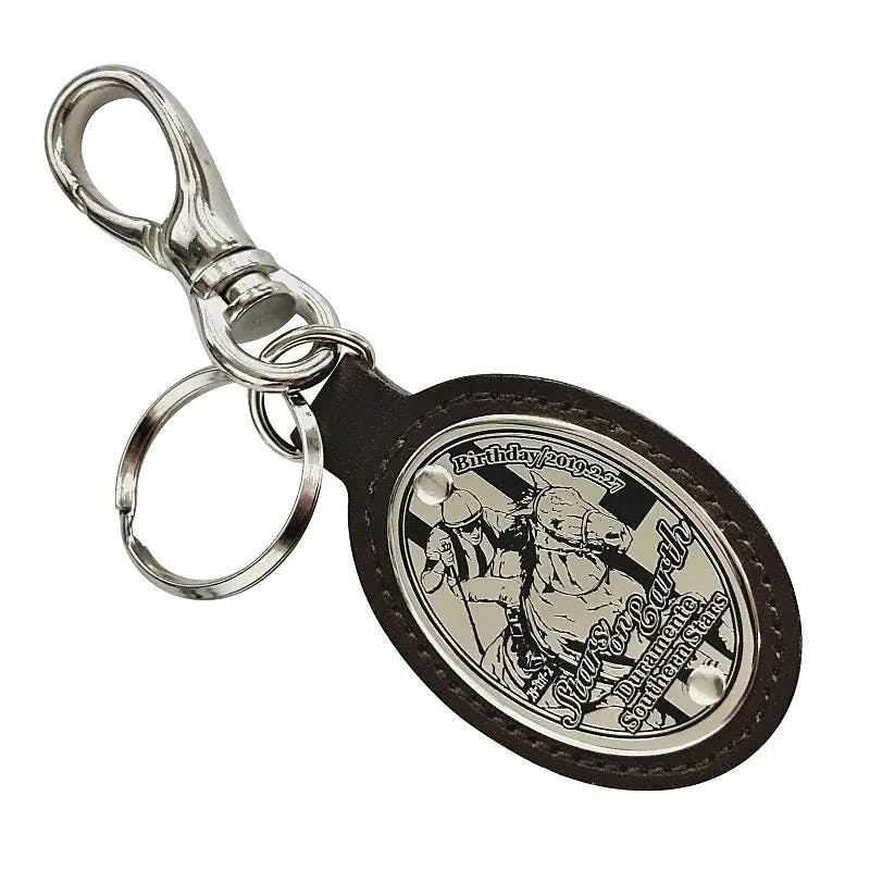Front view of a cow-leather oval keychain with a metal oval plate showing a horse-and-rider illustration and an attached metal clasp and split ring.