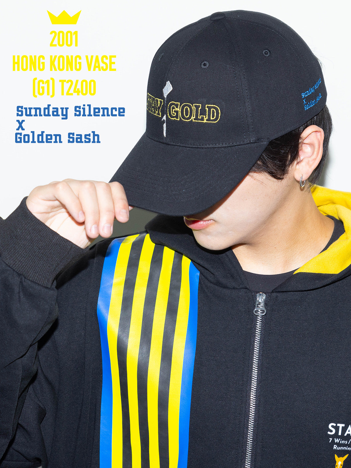 A person wearing a black "STAY GOLD" baseball cap, shown from a front-left angle with their hand touching the brim.