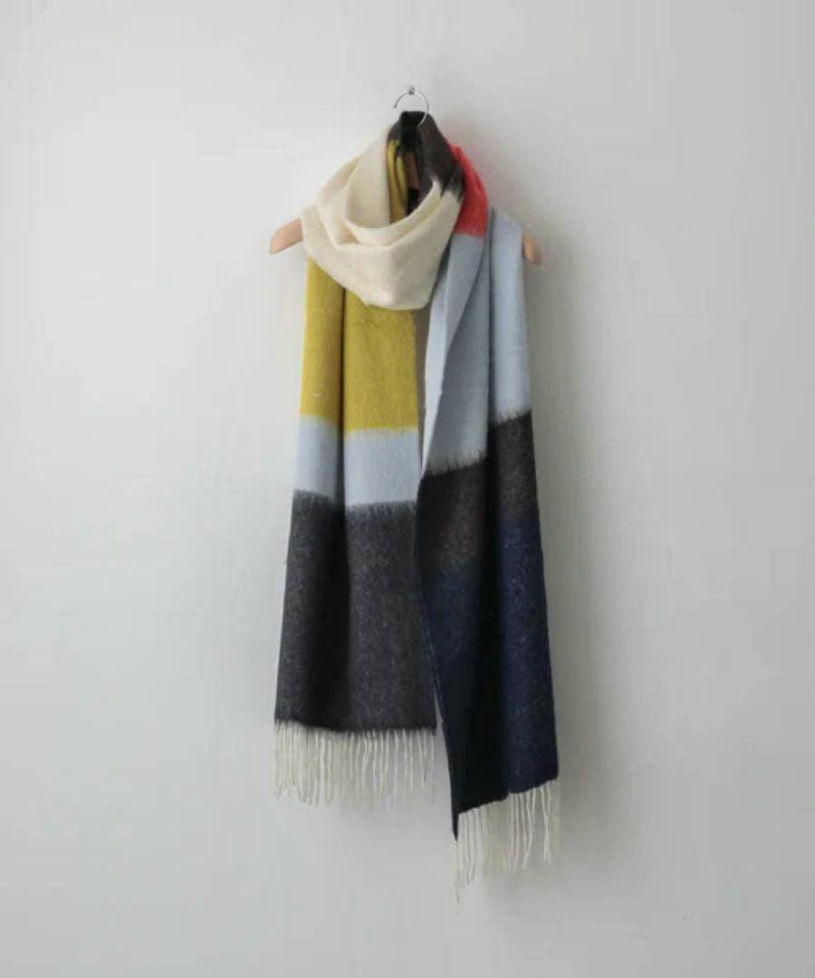 A long alpaca muffler with color-blocked panels and fringed ends hanging from a wall hook.
