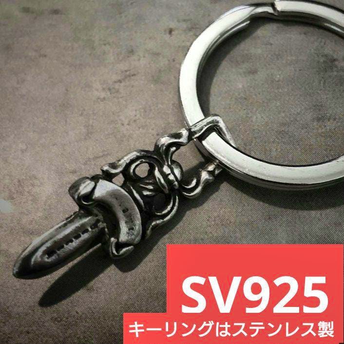 Silver dagger charm attached to a key ring photographed on a gray background.