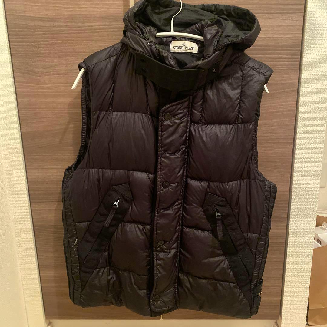 Front view of a black Stone Island down nylon vest with hood and front pockets hanging on a hanger.