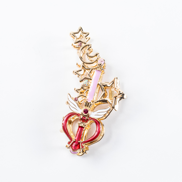 A decorative gold-tone hair clip with star and moon motifs and red and pink enamel details on a white background.