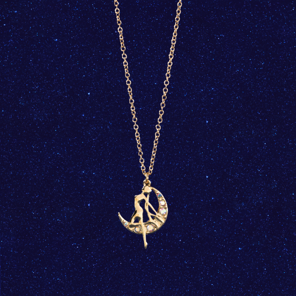 A gold-tone silhouette necklace showing 月野うさぎ (Tsukino Usagi) seated on a crescent moon pendant against a dark blue glittery background.
