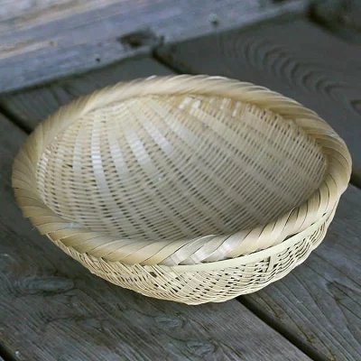 A round woven straw rice-washing basket (sieve) sitting on a wooden surface.
