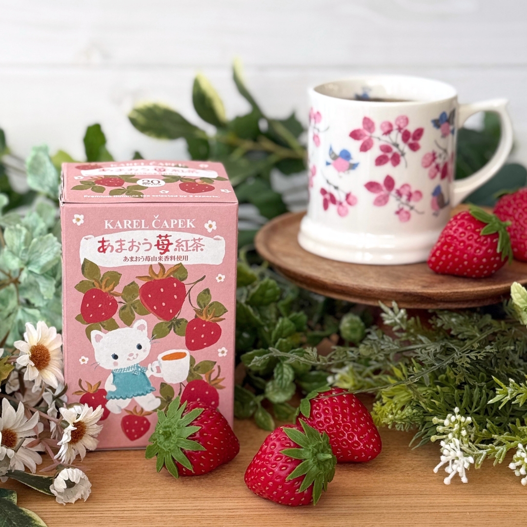 A pink boxed package of strawberry tea bags next to a floral teacup and fresh strawberries.