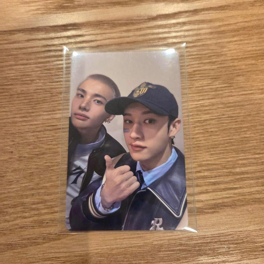 Photocard (Stray Kids unit photocard of Bangchan and Hyunjin) in a clear plastic sleeve placed on a wooden surface.