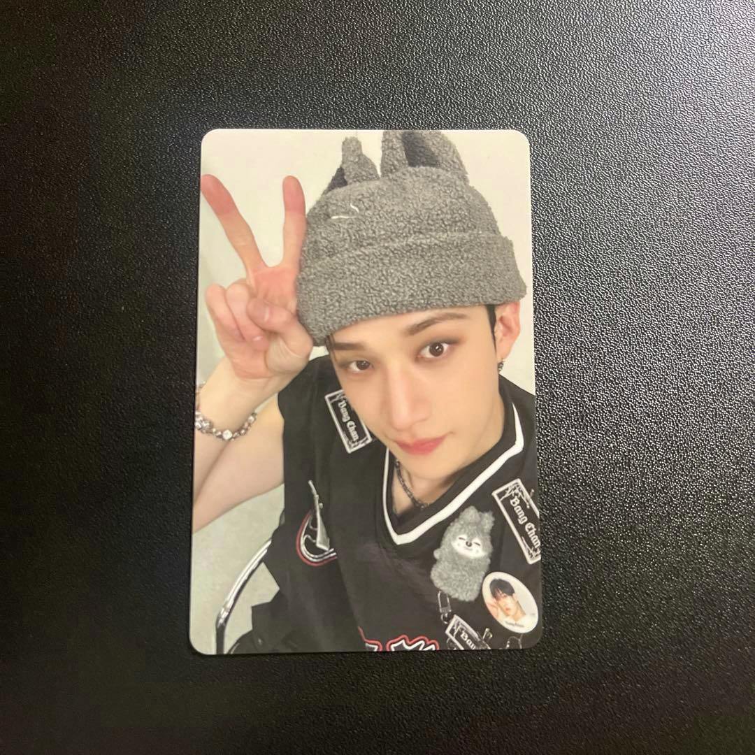 Front of the photocard showing a person wearing a gray knit hat and making a peace sign, placed on a black textured background.