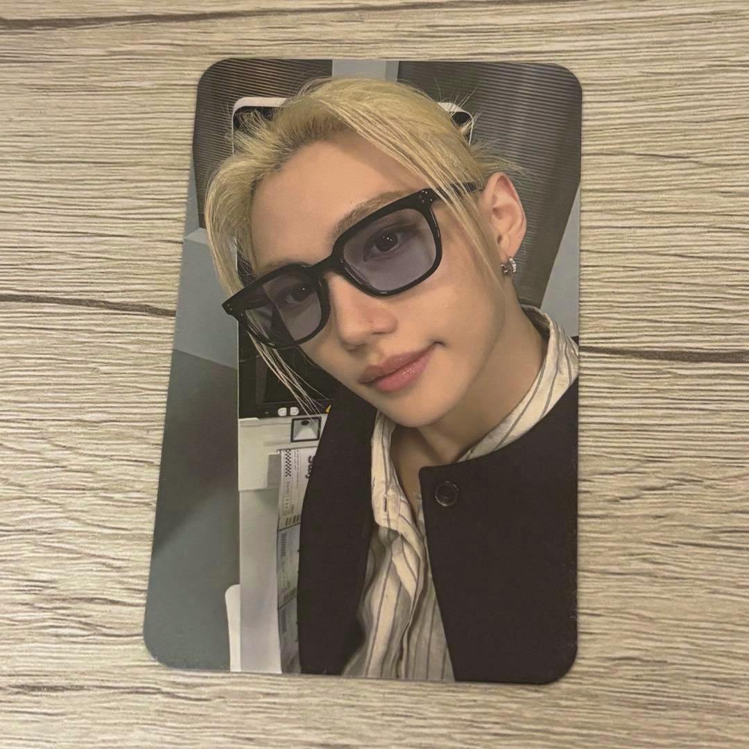 Front of the photocard showing a close-up selfie of a blond person wearing sunglasses on a wooden surface.
