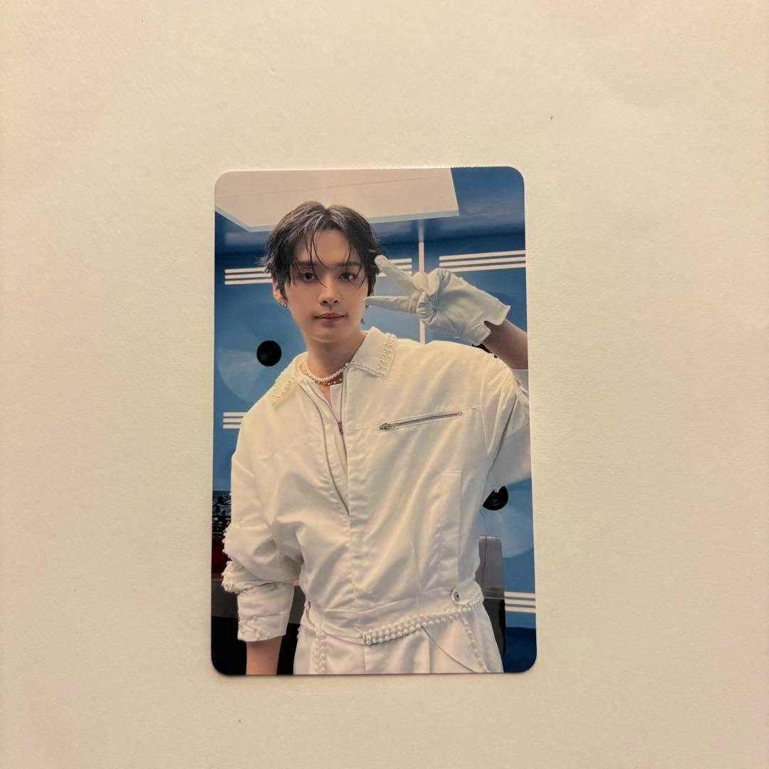 Photo of the StrayKids photocard showing a person in a white outfit and glove making a peace sign against a blue background on a white surface.