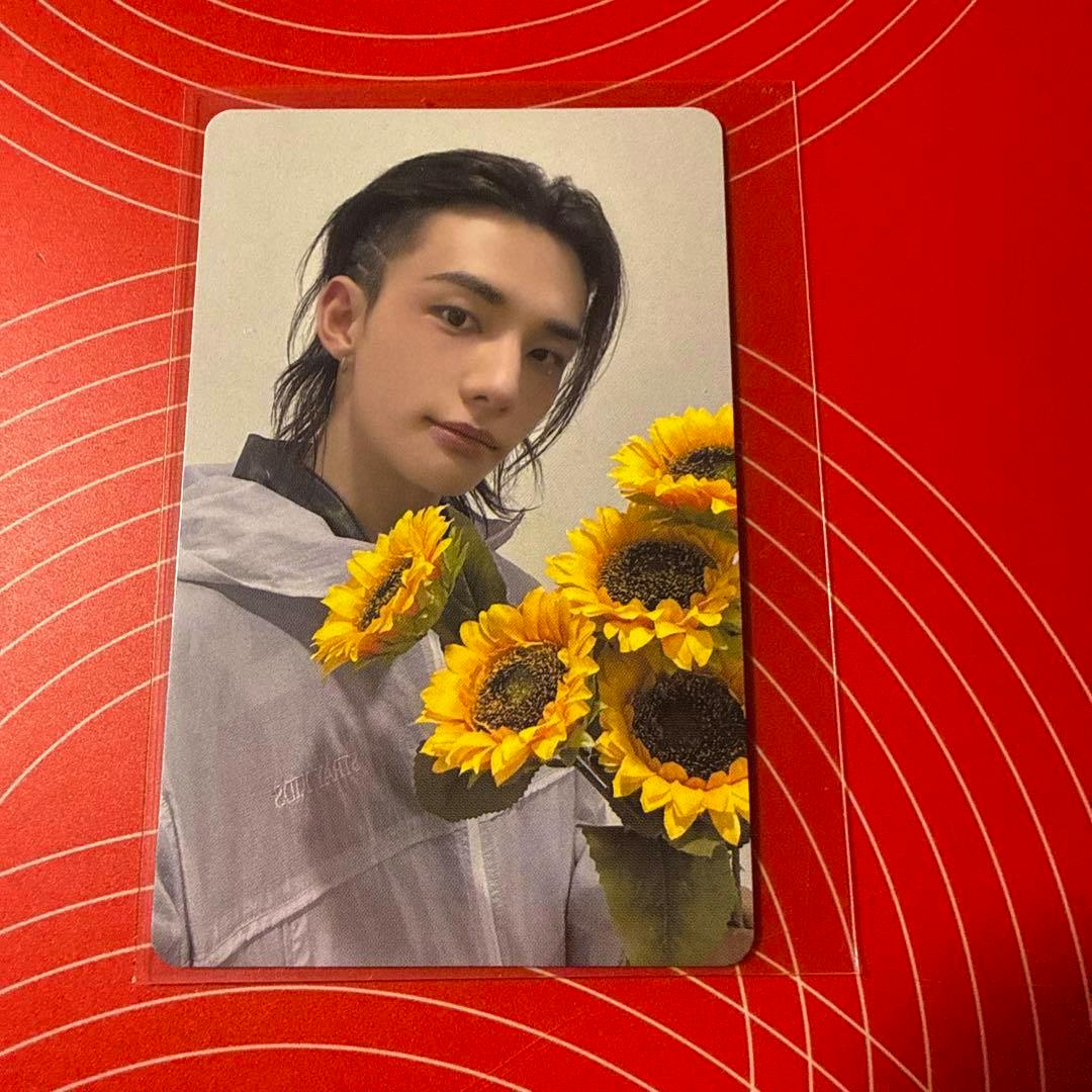 Photocard showing a portrait of a person holding sunflowers on a red patterned surface.