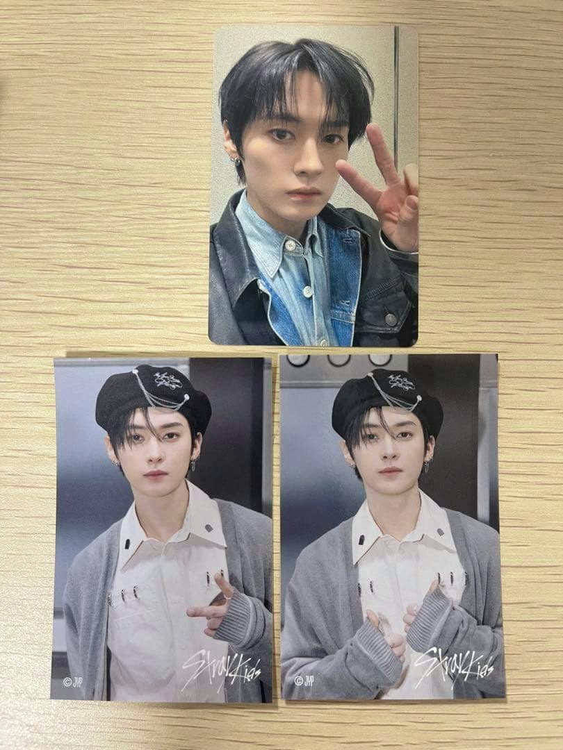 Three StrayKids photocards showing a member in different poses laid out on a wooden surface.