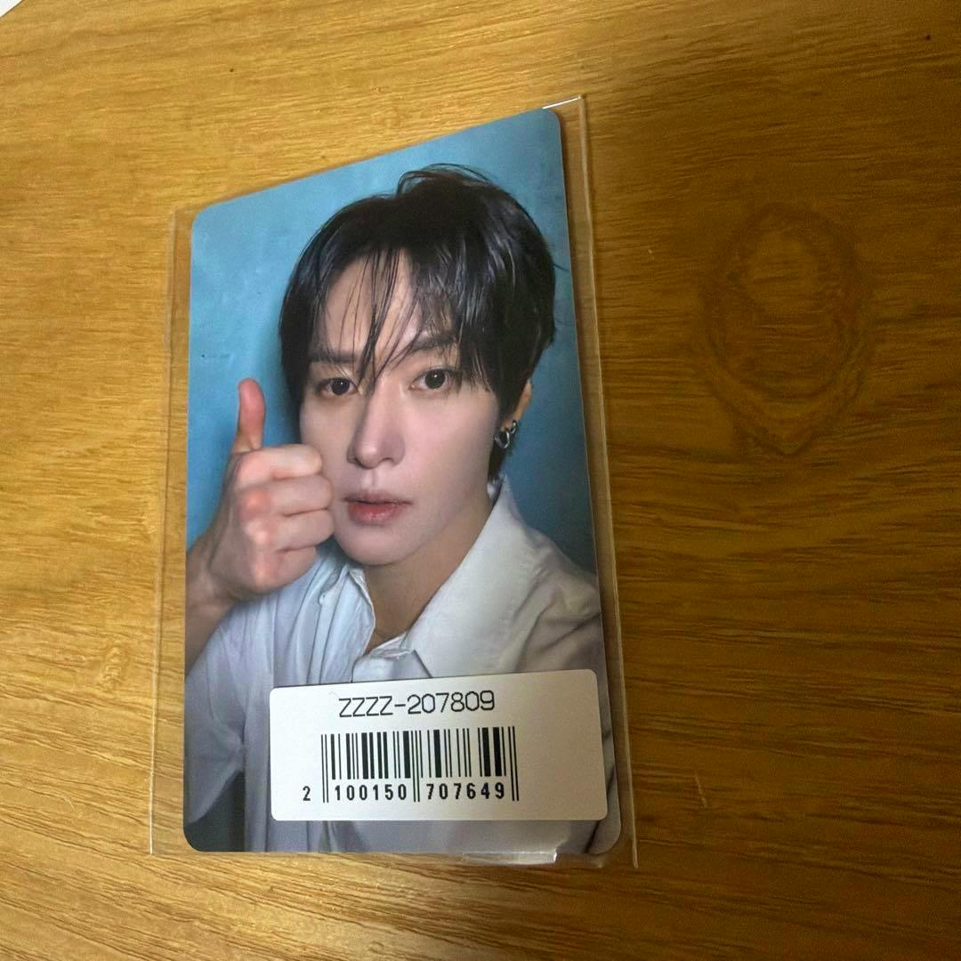 Photocard for straykids リノ (this&that, Sony Music) showing a portrait photocard in a plastic sleeve with the subject giving a thumbs-up and a barcode sticker, placed on a wooden surface.