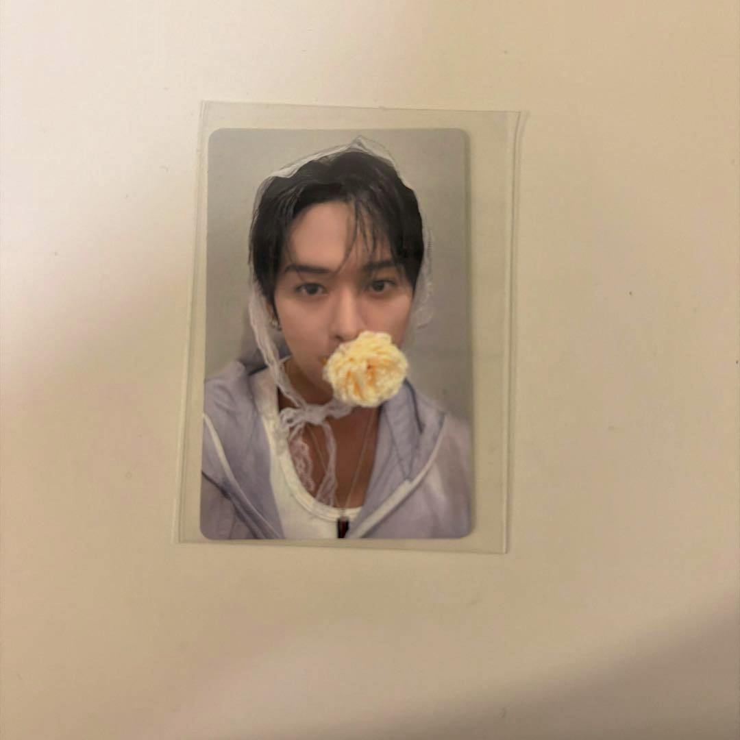 A photocard in a clear protective sleeve showing a person with a flower near their mouth, placed on a white background.