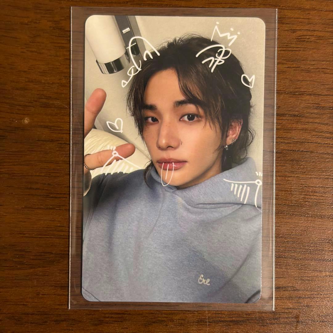Front of the Stray Kids RUN IT JAPAN photocard of Hyunjin showing a close-up portrait with white doodle decorations in a plastic sleeve on a wooden surface.