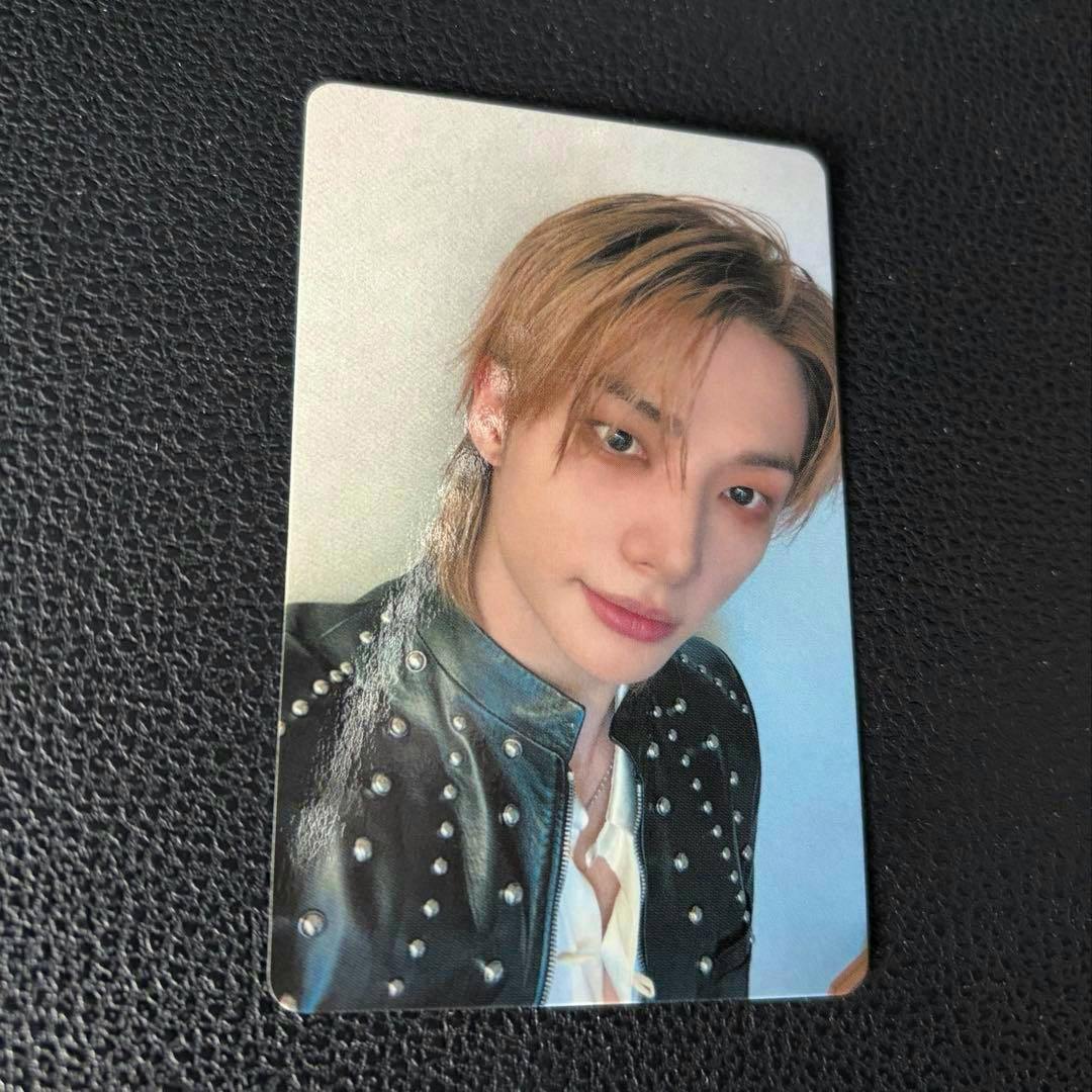 A photocard showing a close-up portrait of a young man wearing a studded leather jacket, placed on a black textured surface.