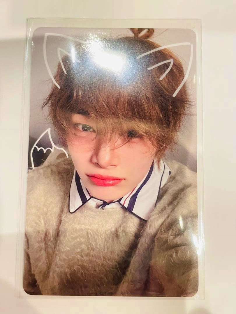 Close-up photocard showing a person wearing a fuzzy sweater with white doodle cat ears drawn on the photo.
