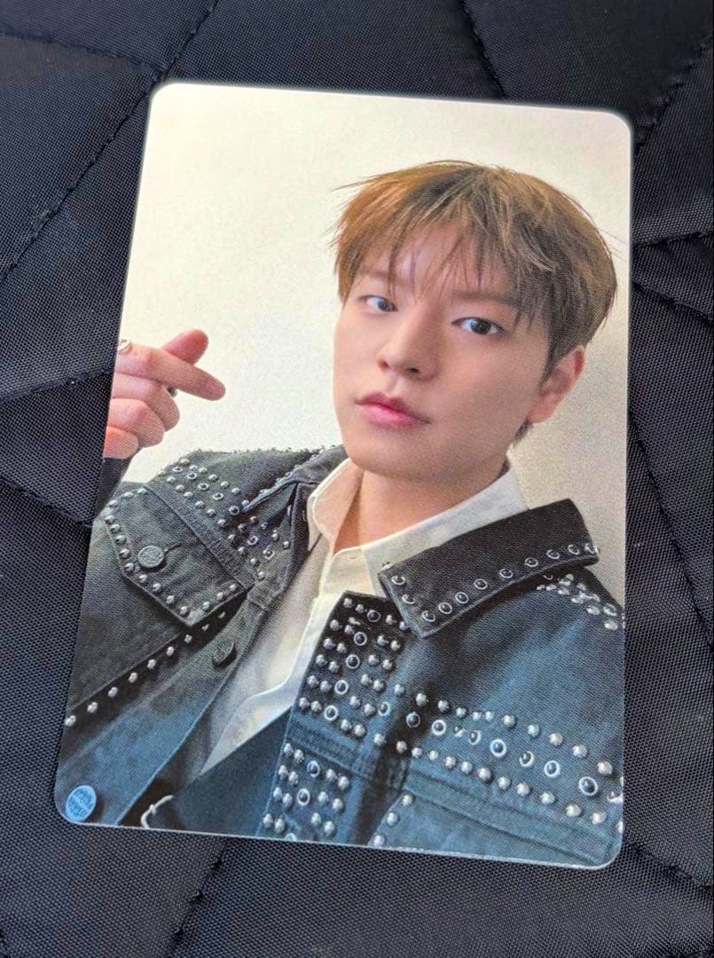 Front of the photocard showing a portrait of a person wearing a studded jacket on a dark quilted surface.