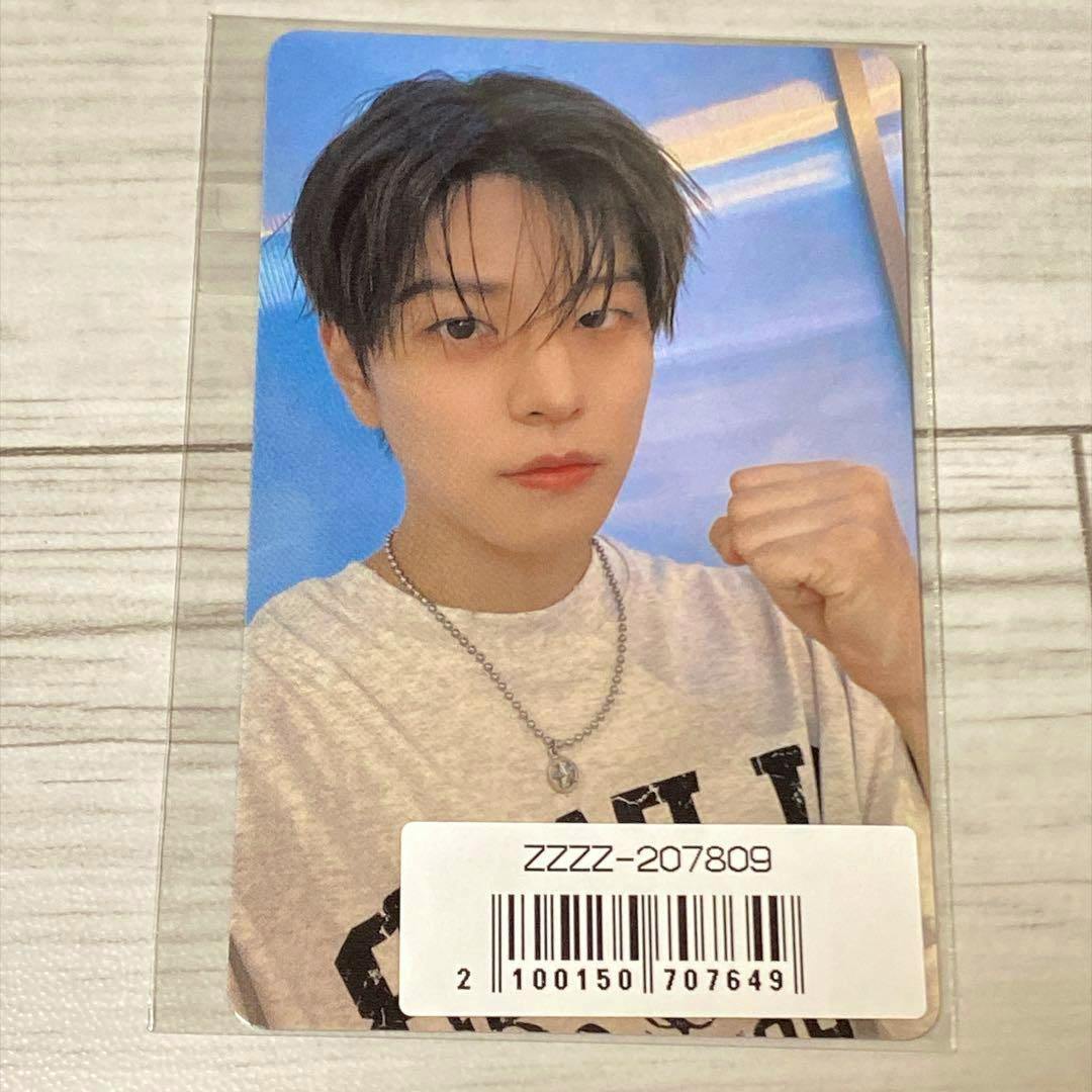 Photocard of Seungmin from Stray Kids in a plastic sleeve with a barcode sticker on the lower front, placed on a light wood surface.