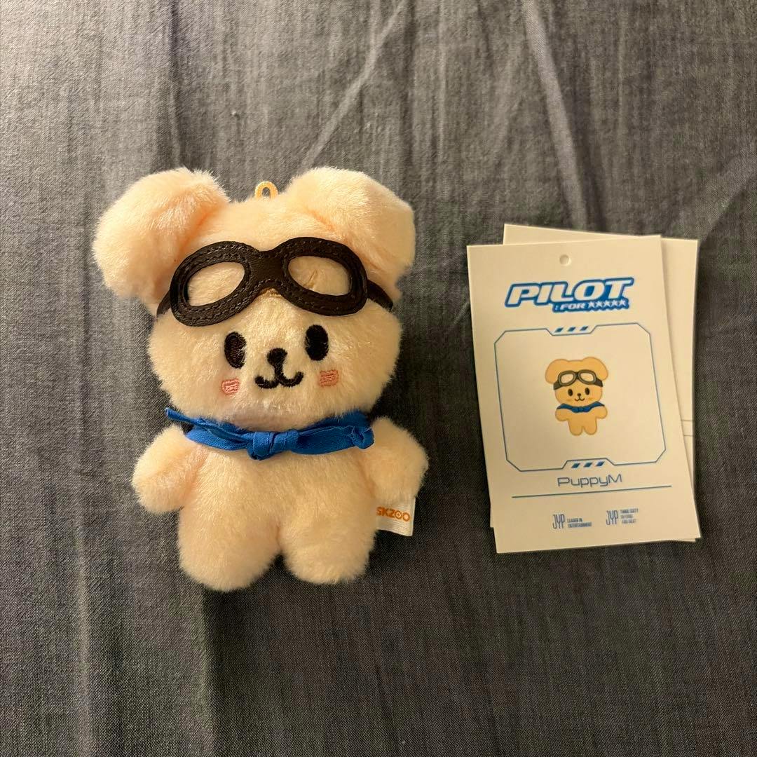 Front view of the Stray Kids SKZOO 10cm pilot plush (パイロット パピーム) wearing goggles and a blue neckerchief with the product tag visible.