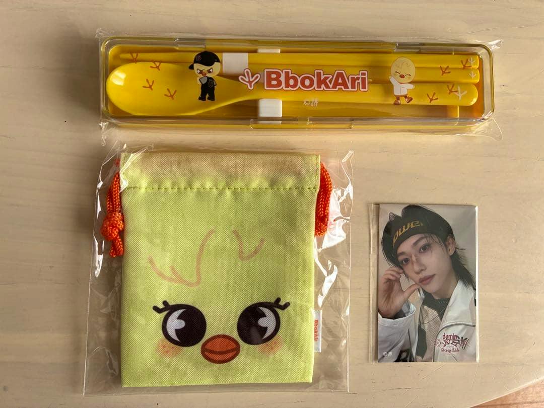 Yellow plastic cutlery case containing a spoon and chopsticks with 'BbokAri' text, a light green drawstring pouch with a chick face, and a small Felix photo card.