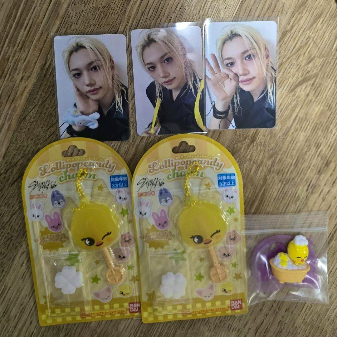 Two packaged yellow lollipop-style acrylic keychain charms and a small loose charm with three Stray Kids photo cards arranged on a wooden surface.
