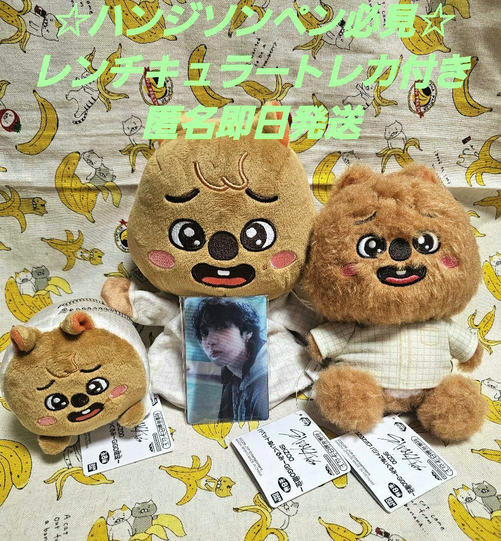 Front view of three Stray Kids SKZOO Han plush dolls with their tags and a trading card arranged on banana-patterned fabric.