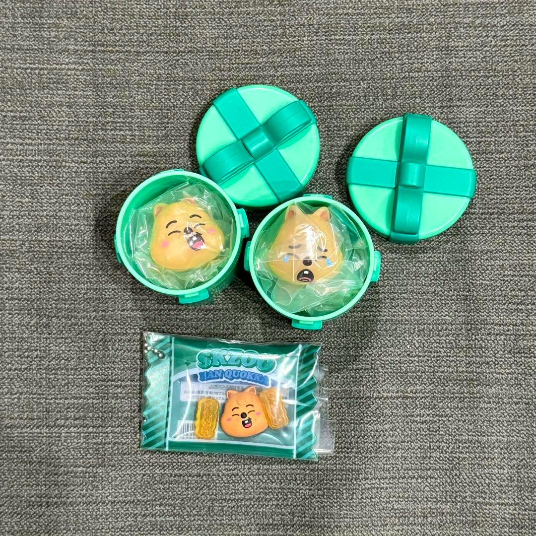 Top-down photo of SKZOO ハンクォッカ plastic charm ring pieces in three green round containers, two open showing character face charms wrapped in plastic and a sealed packaged charm below.