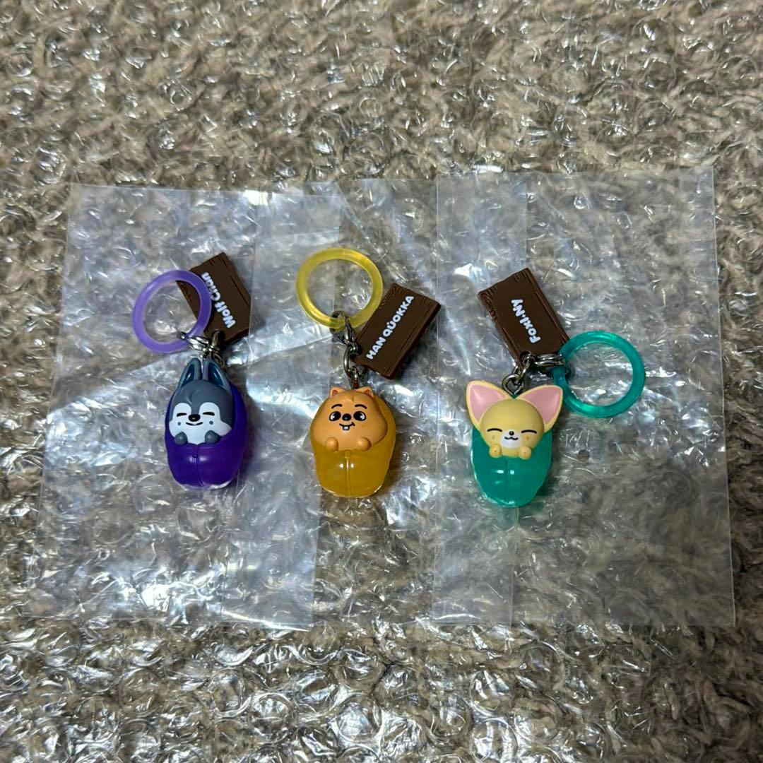 Three SKZOO animal keychain charms in purple, yellow, and teal on colored rings displayed on bubble wrap.
