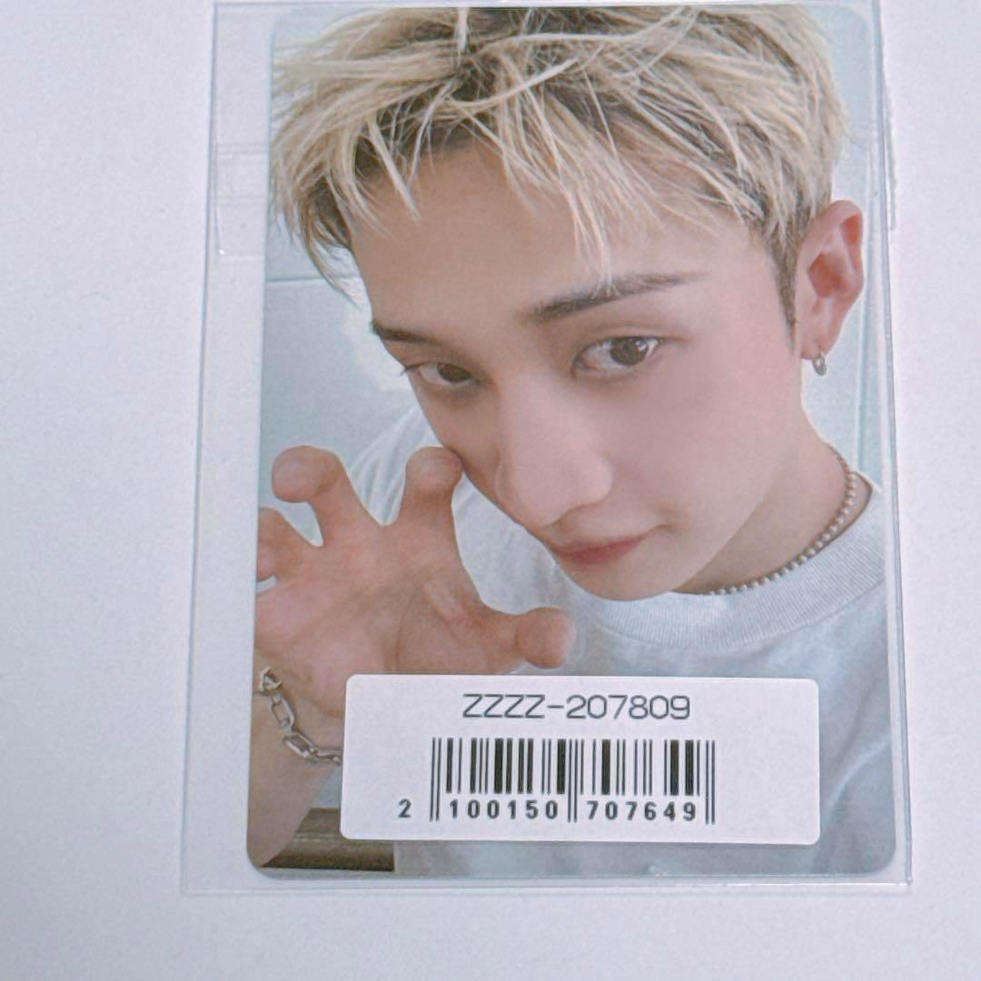 Close-up photocard inside a protective sleeve showing a person making a claw-like hand gesture, with a barcode sticker covering the lower area.