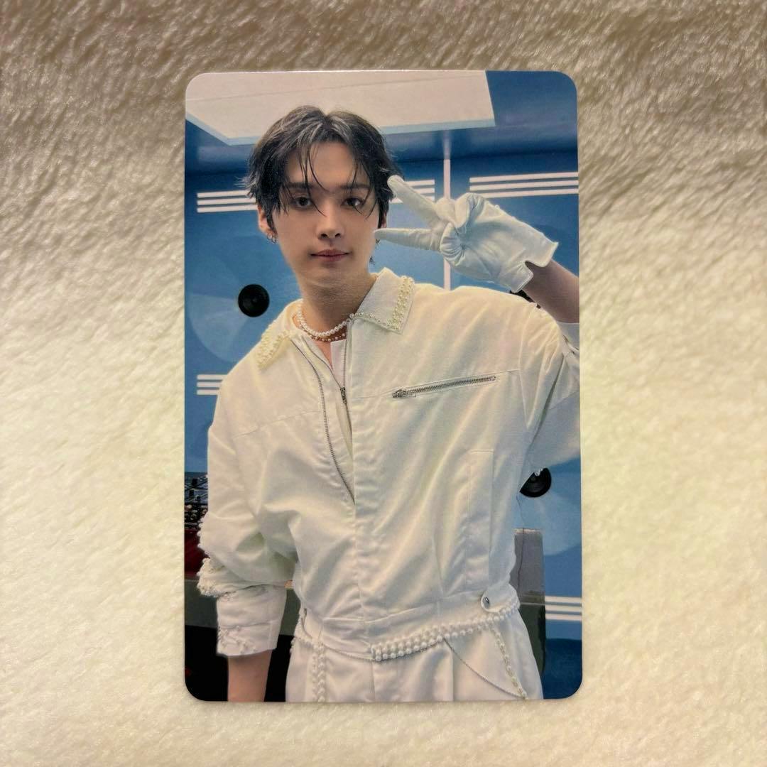 Front of a photocard showing a person in a white outfit making a peace sign against a blue background.