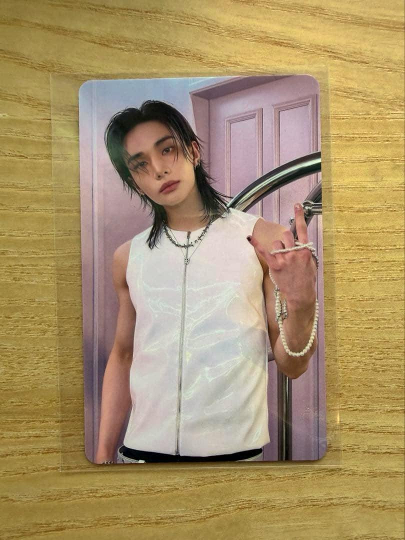 Photocard showing a person wearing a sleeveless white zip-front top and necklaces, photographed on a wooden surface.