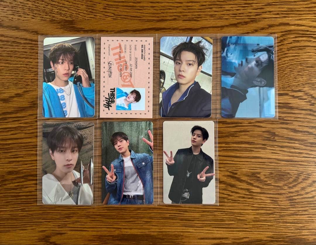 Several Stray Kids "THIS&THAT" photocards laid out in a grid on a wooden surface.