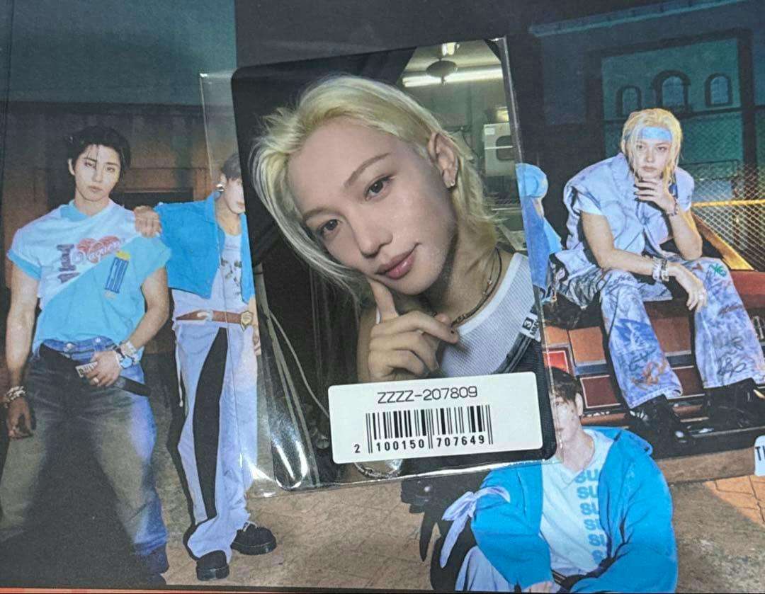 Photocard showing Felix's face from the Stray Kids THIS&THAT set placed on a poster with a barcode sticker partially covering the card.