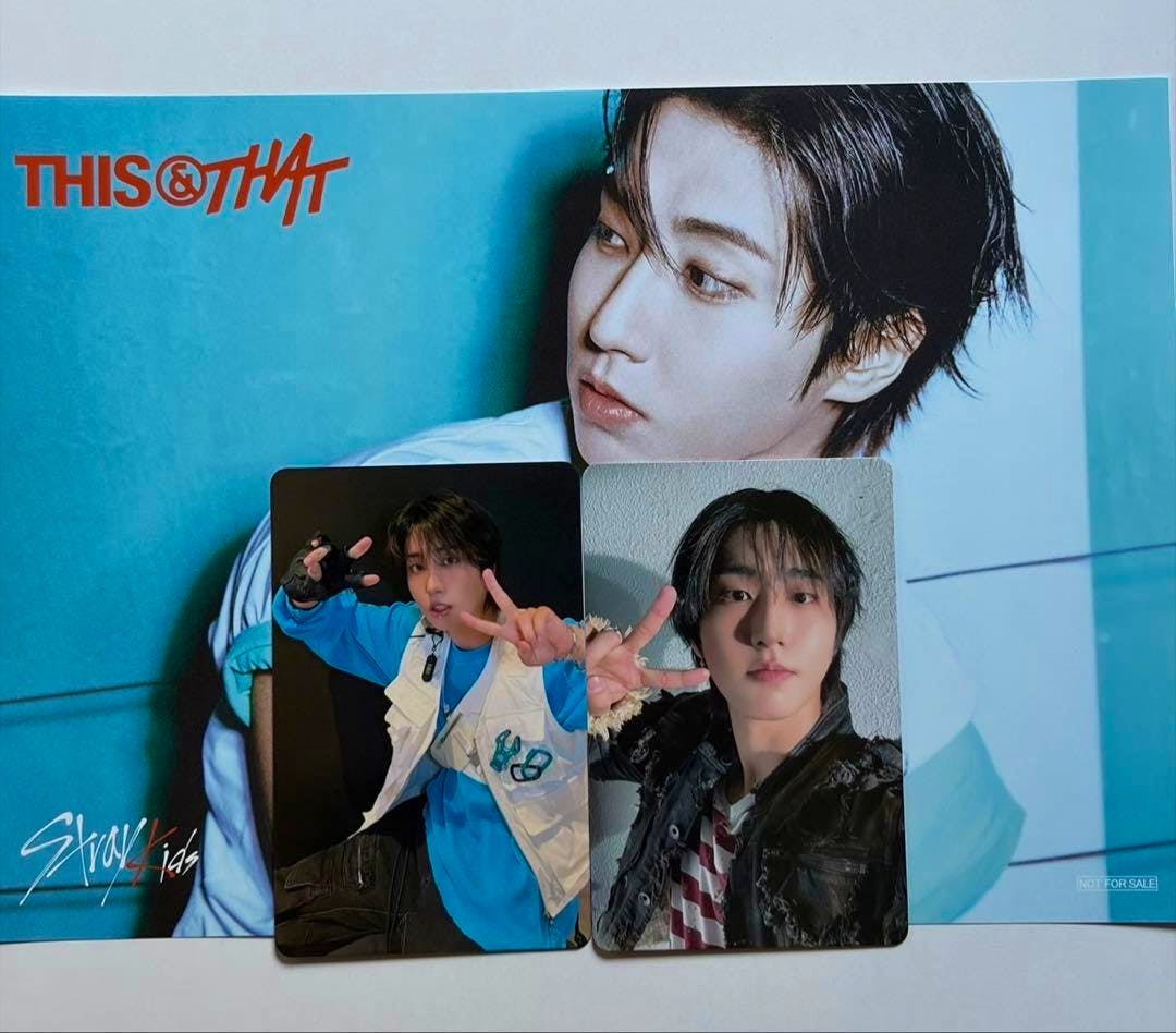 Two Stray Kids photocards placed on a blue THIS&THAT promotional poster showing a member's portrait.