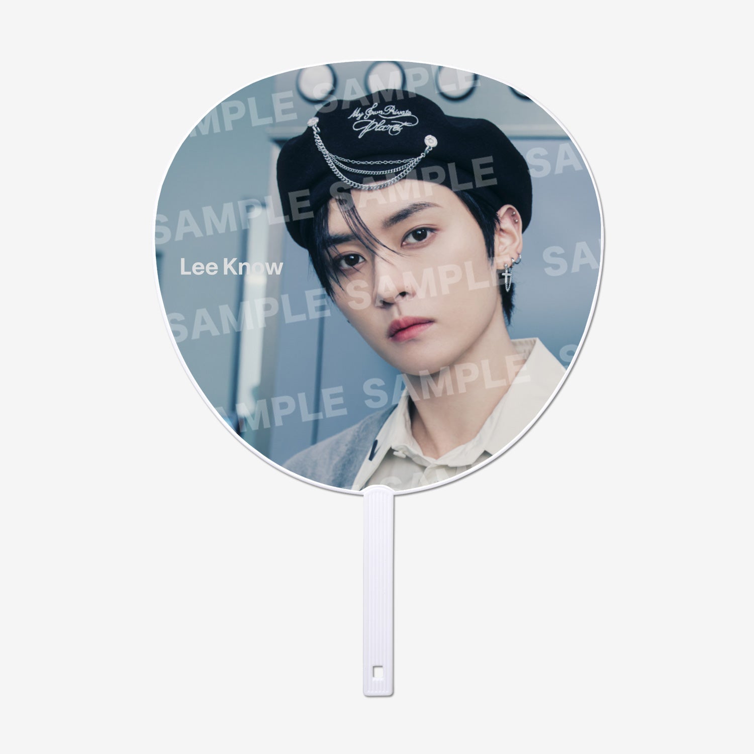 Round paper hand fan showing a portrait photo of Lee Know (Stray Kids) wearing a black hat with chain accessory.
