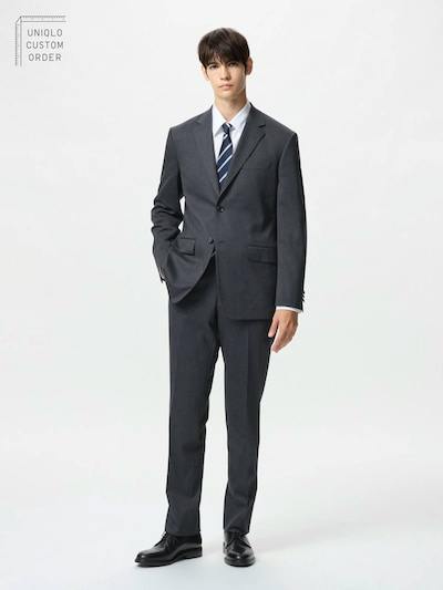 Male model wearing stretch wool pants as part of a dark suit, standing against a white background.