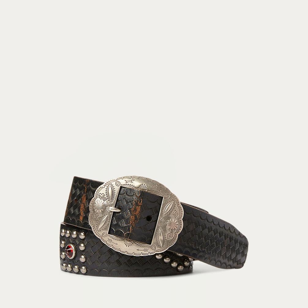 Coiled studded leather belt with woven embossing and a decorative engraved silver-toned buckle on a white background.