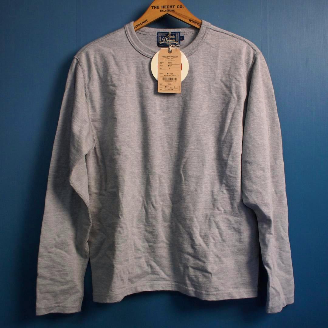 Front view of a heather-gray long-sleeve men's cotton T-shirt hanging on a wooden hanger against a blue background.
