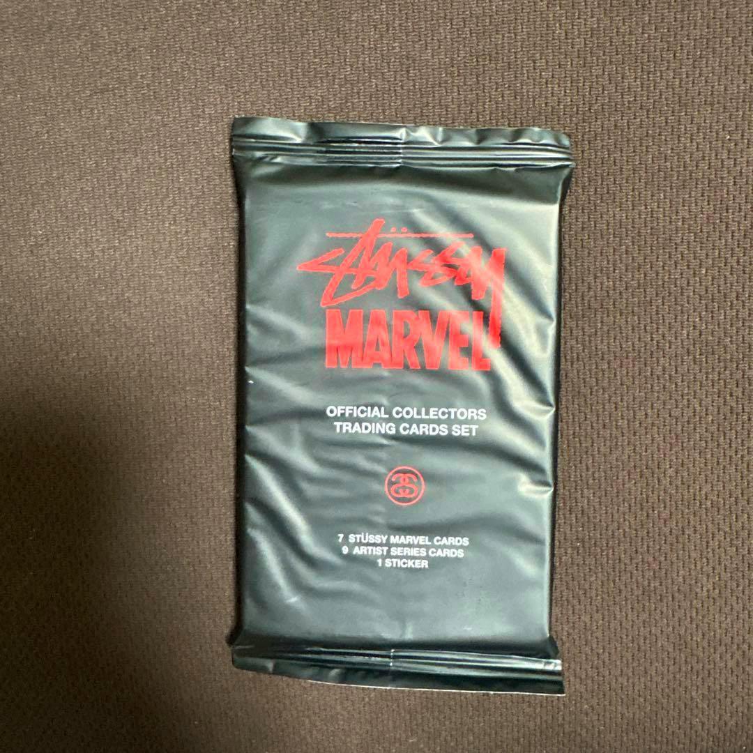 Sealed black STUSSY × MARVEL trading card pack with red and white text on a brown background.