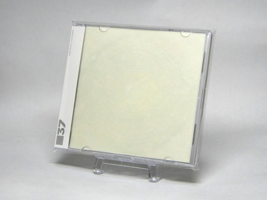A clear CD jewel case standing on a small clear display showing the front insert and spine of the CD case.