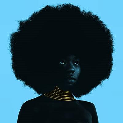Album cover art for Sudan Archives showing a person with a large afro and gold neck rings on a solid blue background.