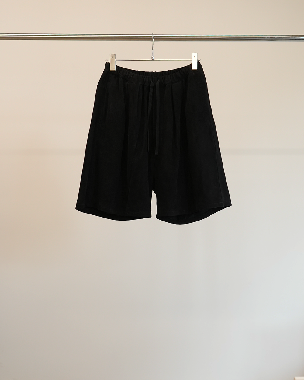 Front view of black suede tuck wide shorts hanging from a clothing rack.