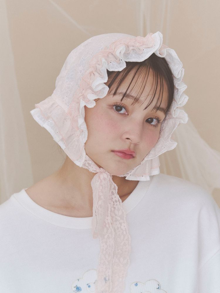 Model wearing a pink lace bonnet tied under the chin.