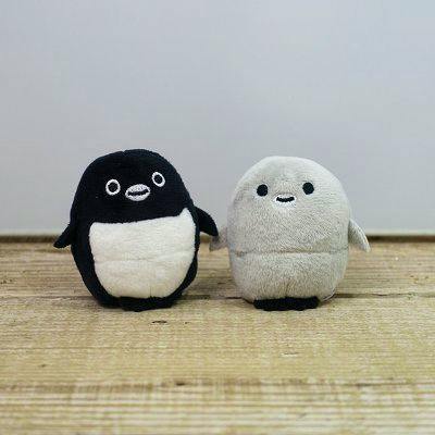 Two Suica penguin plush toys (one black-and-white, one gray) standing on a wooden surface.