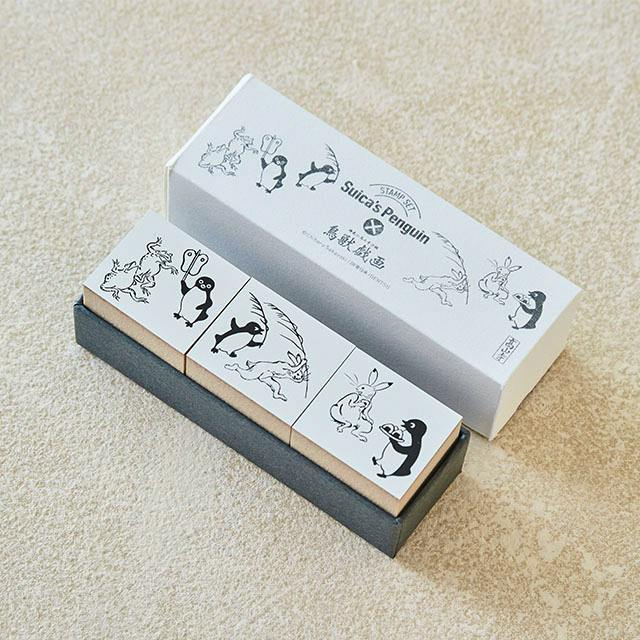 Three wooden stamps from the Suica's Penguin stamp set (Chōjū-giga series) displayed in their box on a textured surface.